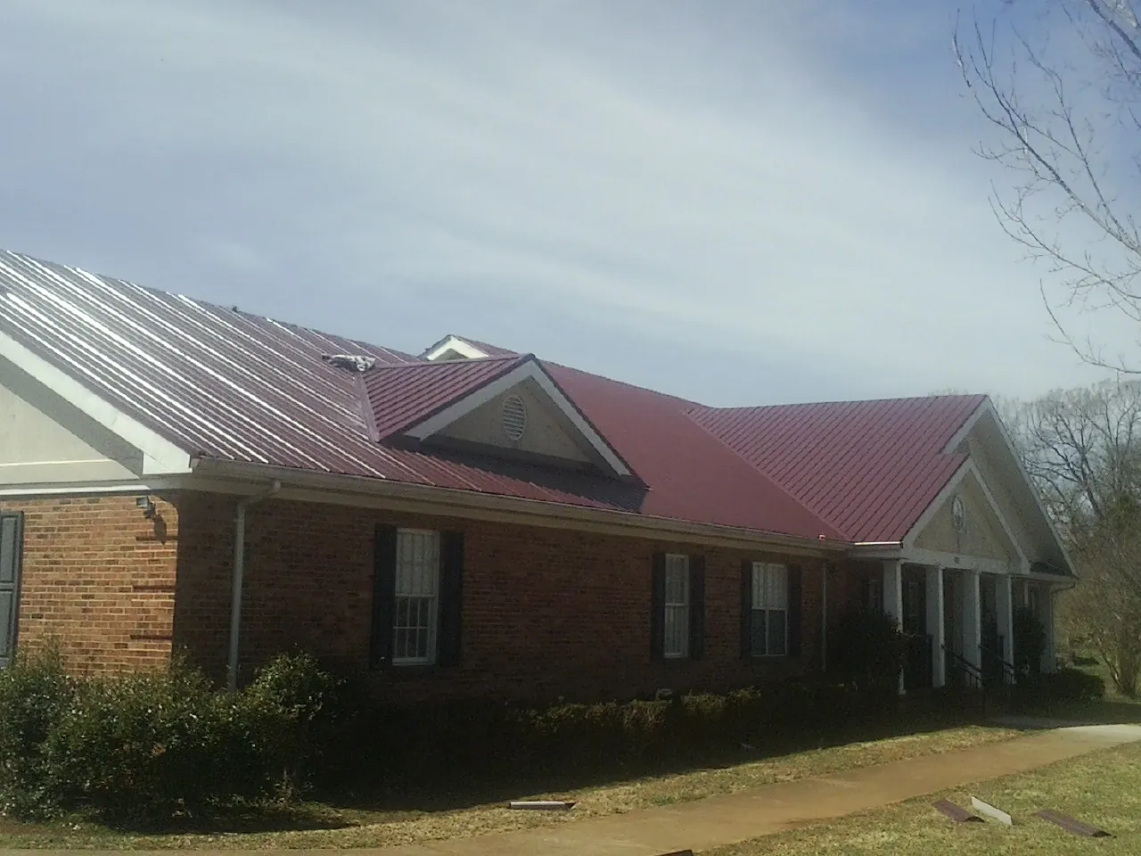 Red metal roof with gabled entries on a long brick building, from a Hail Damage Roof Repair job in University Place