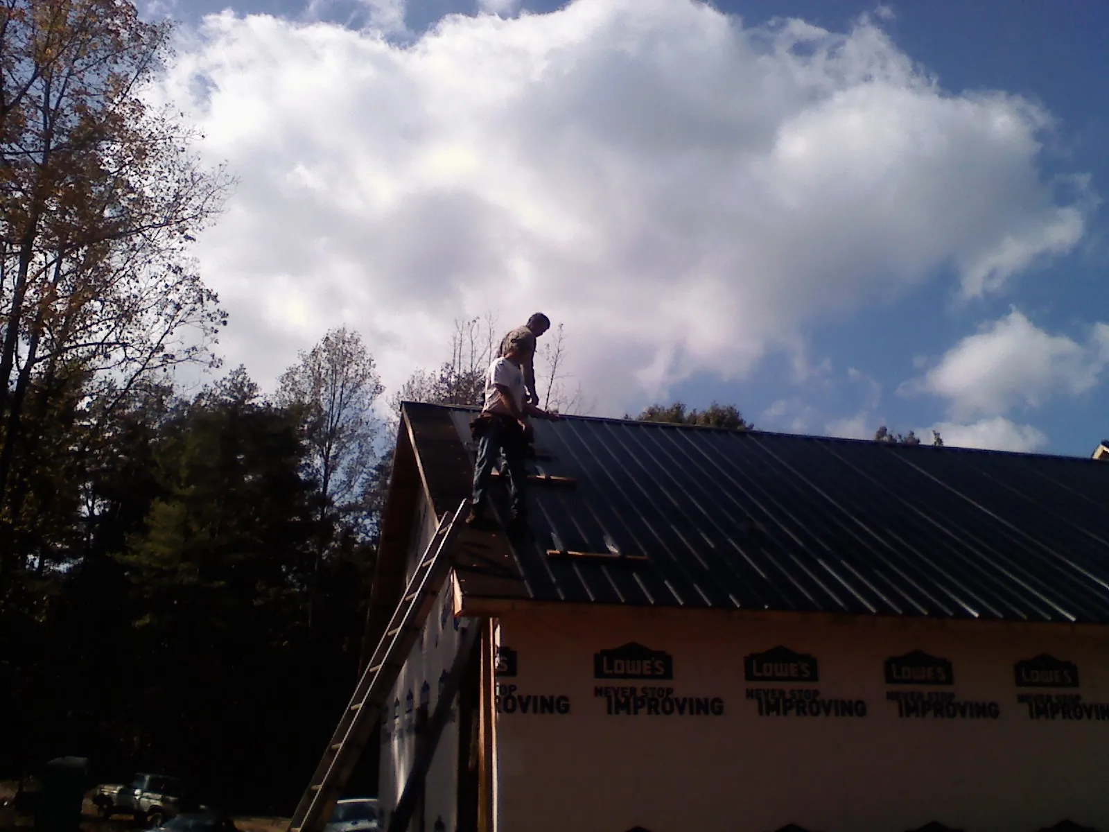 Roofer fastening dark metal panels high against a cloudy sky, from a Roof Inspection job in University Place