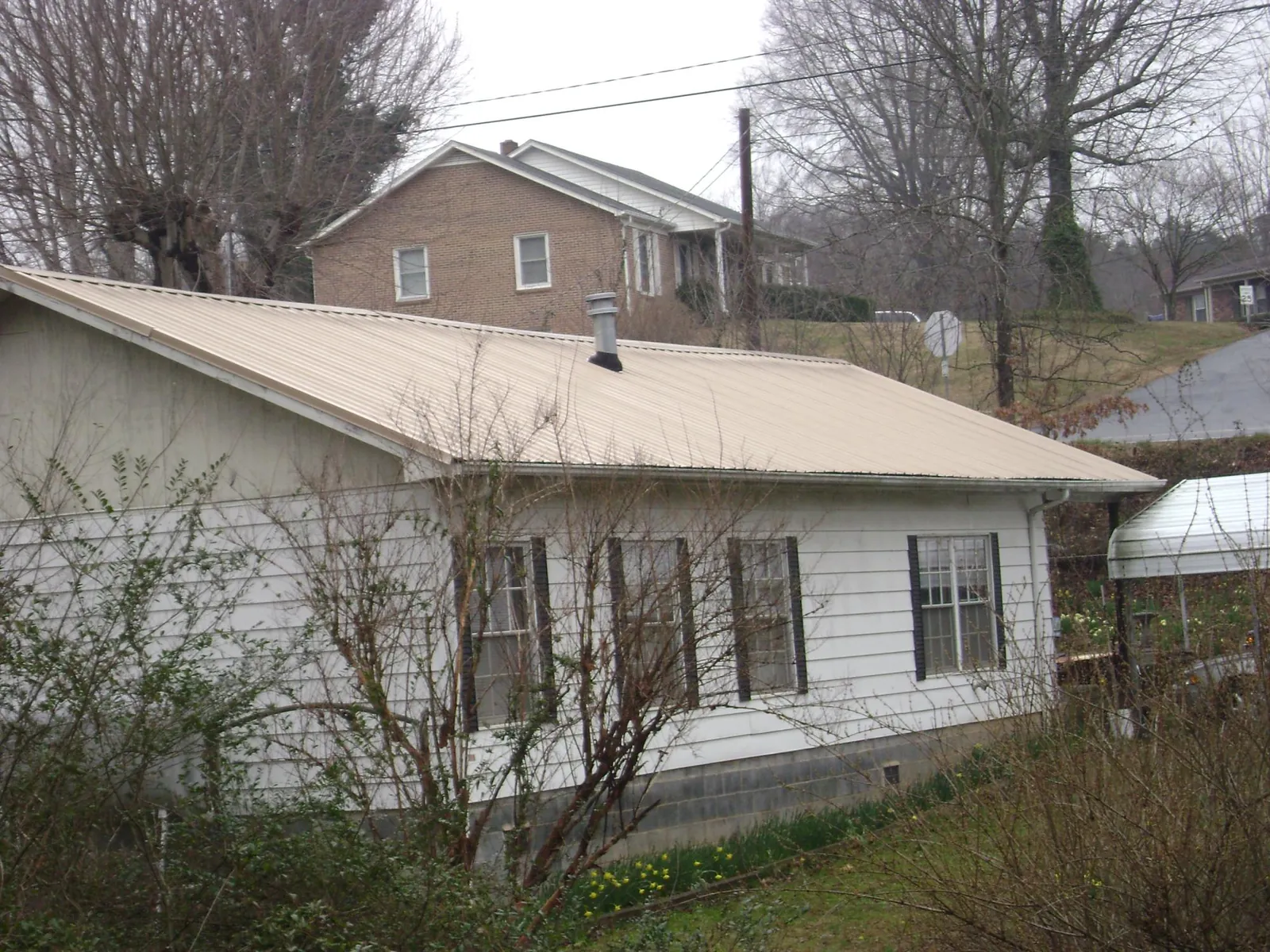 Tan metal roof on a white sided house set into a hillside — Commercial Roofing by Roofing Brothers in University Place